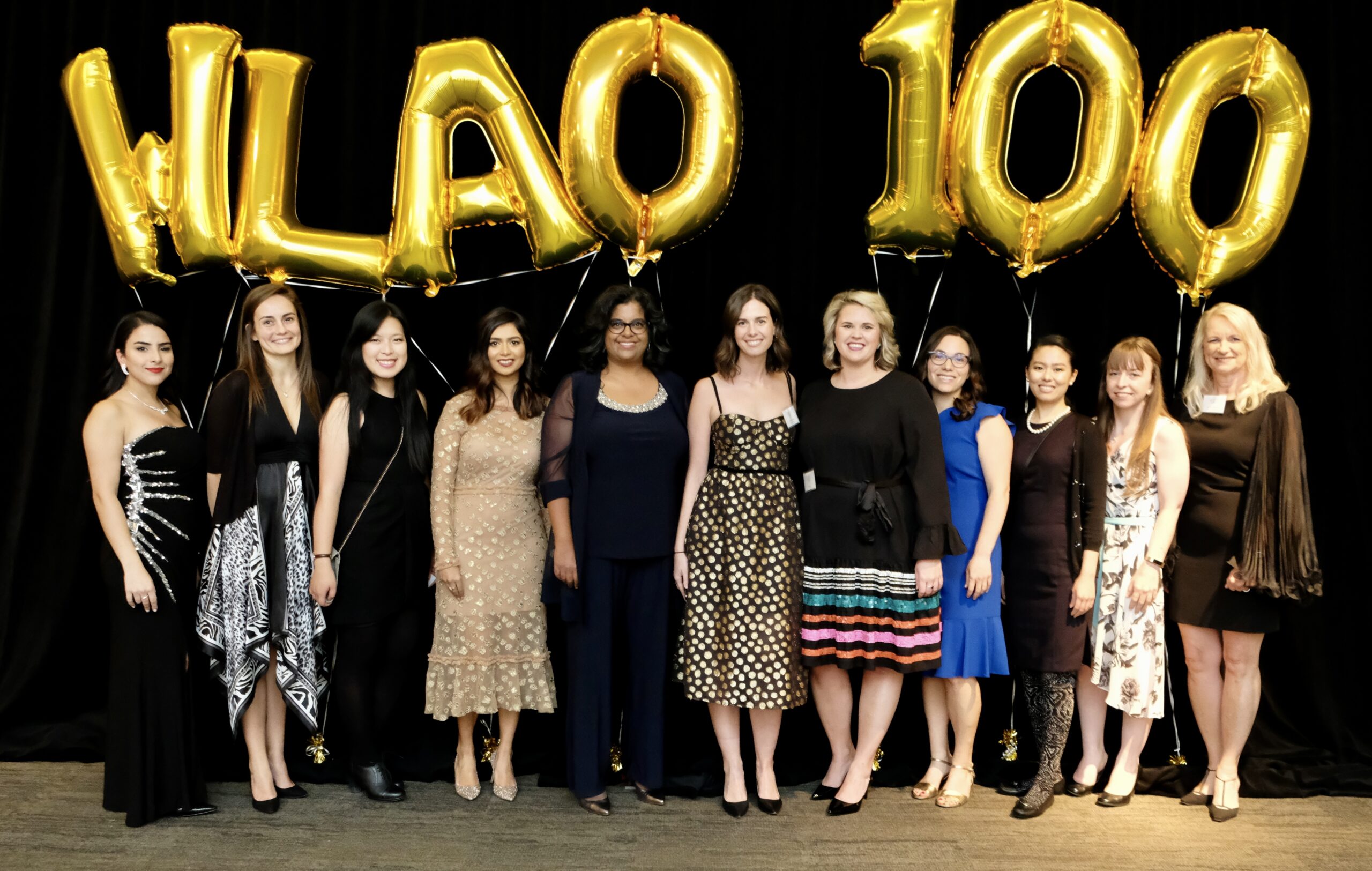 Ten women lined up in celebration of 100 years of the WLAO, with balloons depicting "100 years" floating above them.